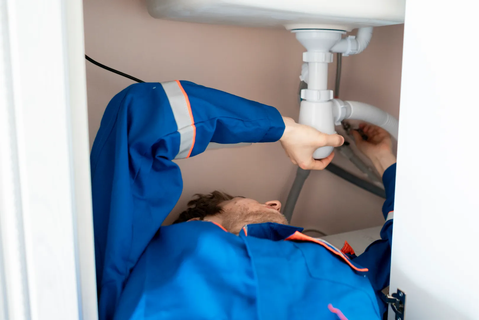 Drain Cleaning and Clog Removal, Licensed Kitchen Drain Plumber Toronto GTA Licensed plumber in blue uniform clearing kitchen drain, professional drain cleaning service across Toronto and GTA
